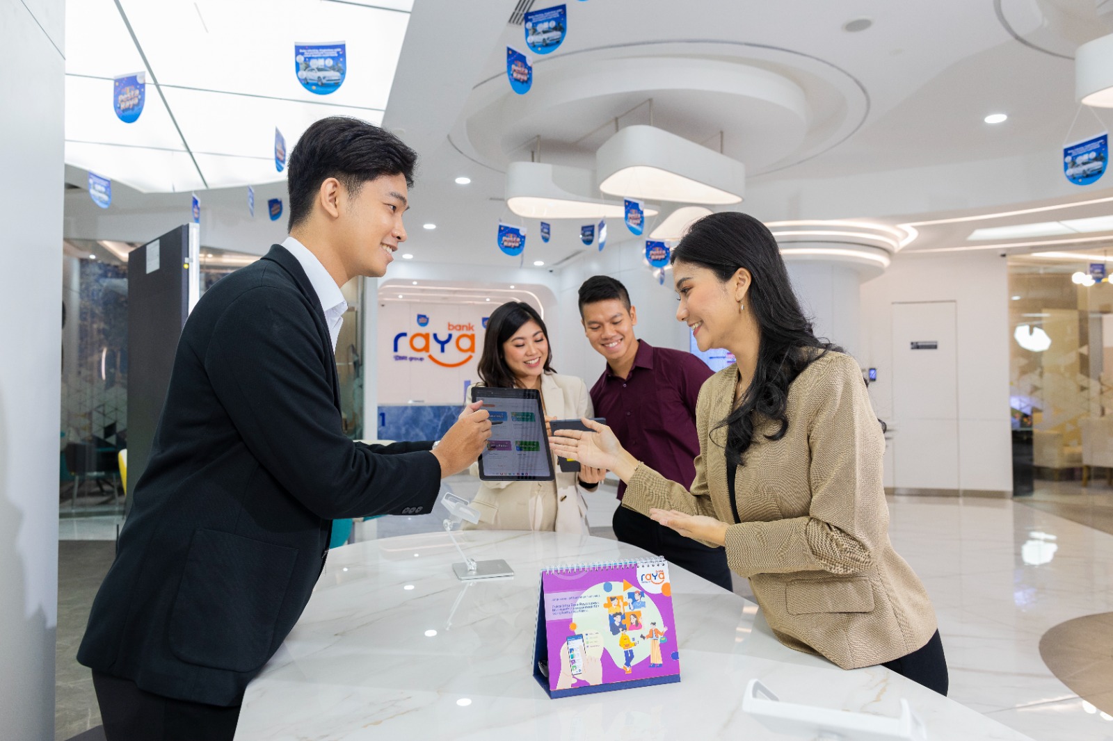 Simulasi pelayanan nasabah oleh pegawai PT Bank Raya Indonesia Tbk. (AGRO) terus adaptif dengan transformasi juga supremasi digitalisasi melalui aplikasi digital saving Raya App. Platform aplikasi ini dirancang solutif dalam pemecahan masalah finansial terpadu, mulai dari menabung, transaksi perbankan, pembayaran, pinjaman, hingga investasi. Per Juni 2025, Raya App telah mengoleksi 83 fitur, termasuk Saku Bujet, Saku Pintar, Saku Jaga, Saku Bisnis, QRIS Bisnis, dan Saku Bareng untuk tabungan kolekqq,{}tif komunitas. Dengan bobot aplikasi yang ringan juga latar muka (user interface/UI) intuitif, nasabah dapat menyesuaikan menu sesuai preferensi. Aspek keamanan juga menjadi prioritas melalui two-factor authentication serta fitur pengamanan transaksi agar nasabah dapat membatasi nominal sesuai ketentuan pribadi. Kicky Andrie Davetra, Direktur Bisnis Bank Raya, mengatakan, “Dalam berinovasi, Bank Raya berupaya untuk menghadirkan produk perbankan digital yang built-to-last, sehingga produk yang dihadirkan tidak lekang oleh waktu karena fungsinya yang selalu relevan dan memenuhi kebutuhan masyarakat dalam bertransaksi perbankan, serta mudah dan reliable.” Sejak diluncurkan pada 2022, Raya App mencatat 2,1 juta transaksi per Juni 2025 atau naik 42,7% (yoy), dengan pengguna lebih dari 1,05 juta nasabah. Dana simpanan digital tumbuh 66,6% menjadi Rp1,5 triliun, mendorong kenaikan CASA 7,6% (yoy) menjadi Rp2,5 triliun dan rasio CASA naik ke 29,72% pada Kuartal II/2025. Kicky menambahkan, “Fitur Saku sebagai champion product di Raya App dikembangkan menyesuaikan dengan kebutuhan masyarakat saat ini agar menabung maupun bertransaksi perbankan dapat lebih mudah dan nyaman.” Selain fitur Saku, Raya App menawarkan layanan QRIS, top up e-wallet, pembelian pulsa, token listrik, pembayaran tagihan, setor dan tarik tunai di ATM BRI, Agen BRILink, hingga jaringan Indomaret. Inovasi terbaru mencakup Buy Now Pay Later (Raya Paylater) dan “Raya Story”, fitur ringkasan keuangan interaktif layaknya story media sosial. “Untuk mewujudkan semangat kami menjadi digital attacker BRI Group, kami terus menciptakan teknologi yang mendorong kemajuan nasabah secara inklusif, serta secara bersamaan terus meningkatkan user experience seluruh pengguna Raya App,” ujar Kicky. Bank Raya (AGRO) Kembangkan Raya App sebagai Produk Built-to-Last